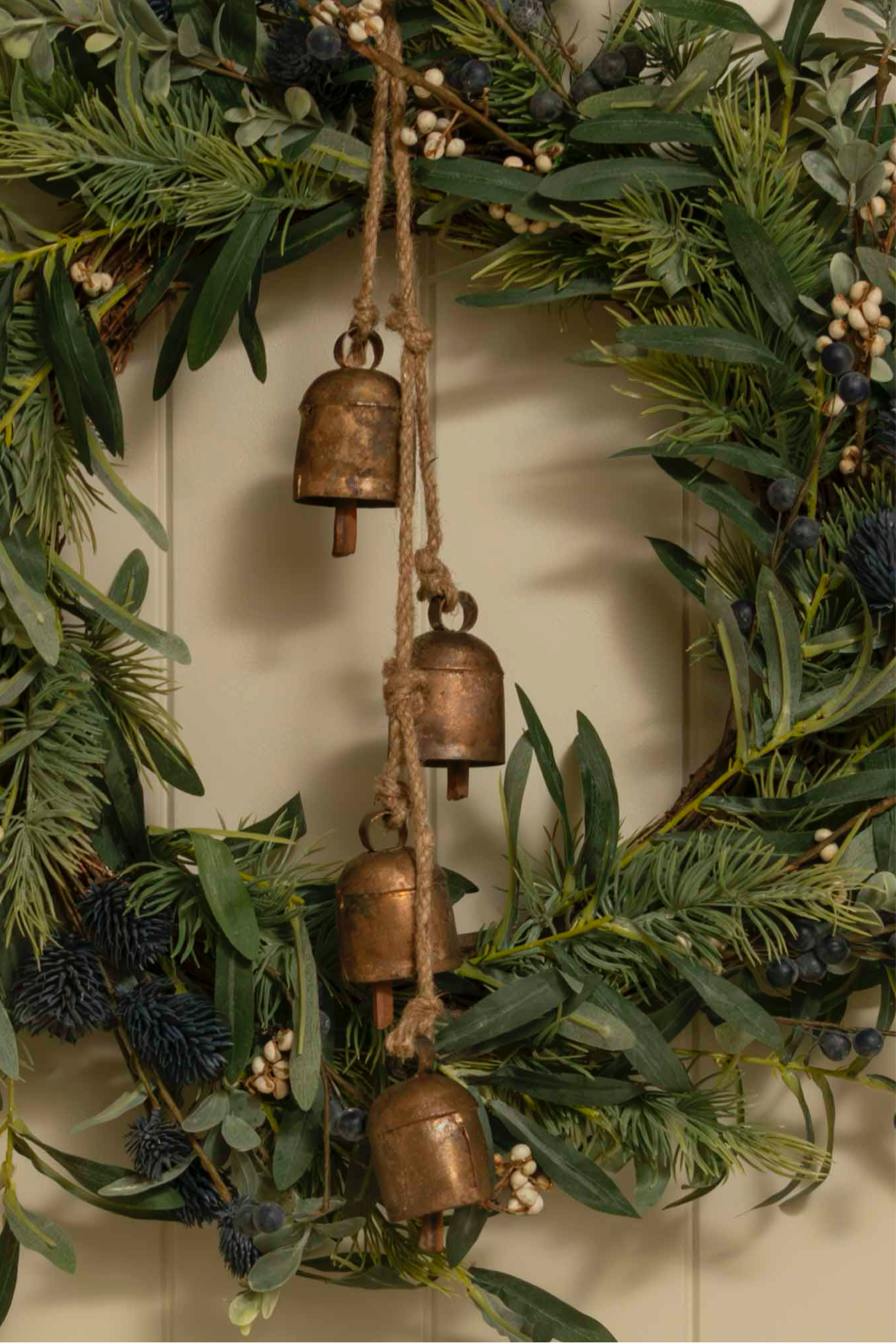 Decorative wreath with greenery and bronze bells on a neutral background
