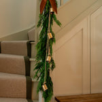 Vintage brass bell cluster hanging on natural jute string with greenery and bow on staircase railing