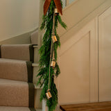 Vintage brass bell cluster hanging on natural jute string with greenery and bow on staircase railing