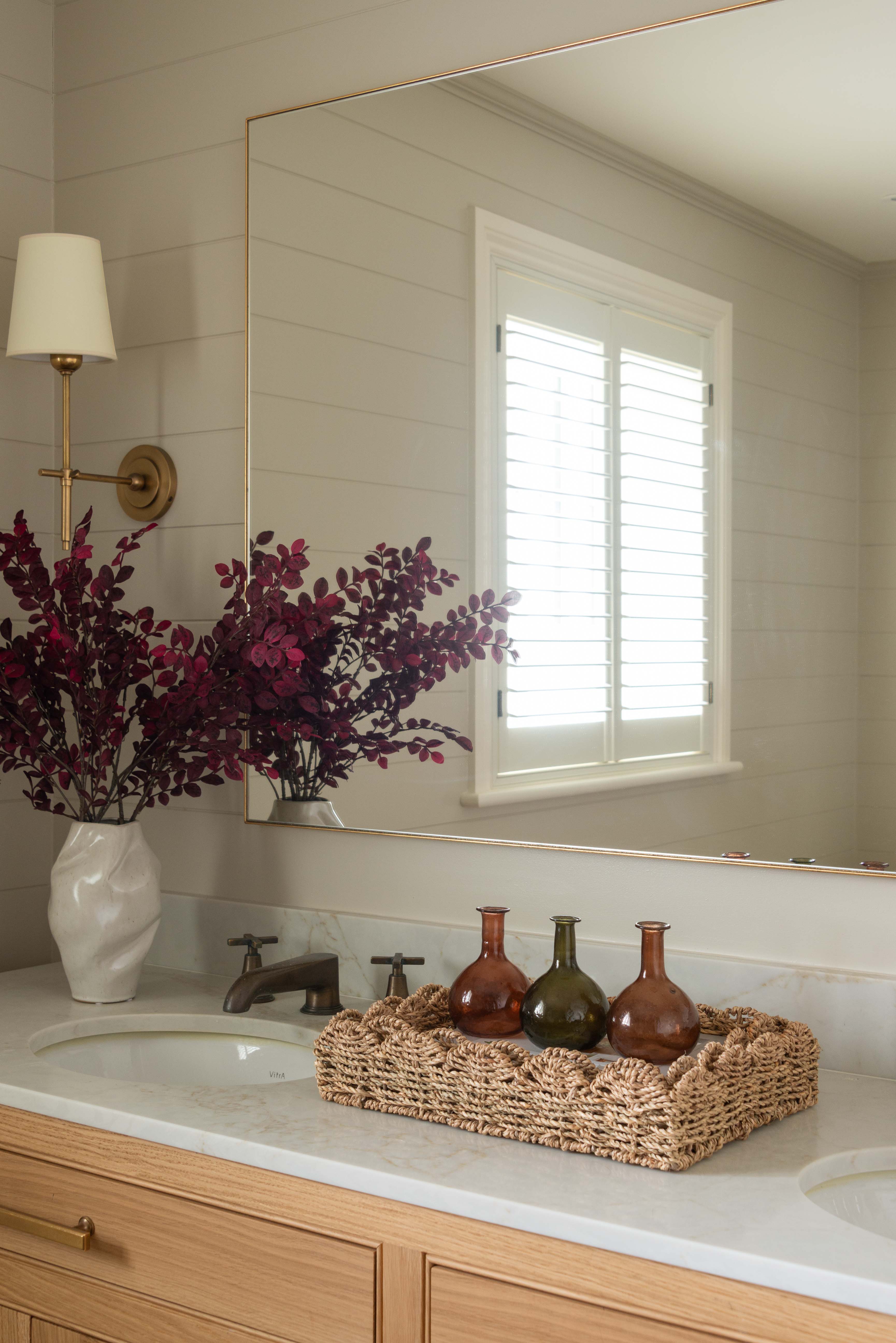 Bathroom vanity with a mirror, vase of flowers, and decorative bottles.