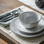 Set of white ceramic bowls on a wooden table with cutlery and a napkin.