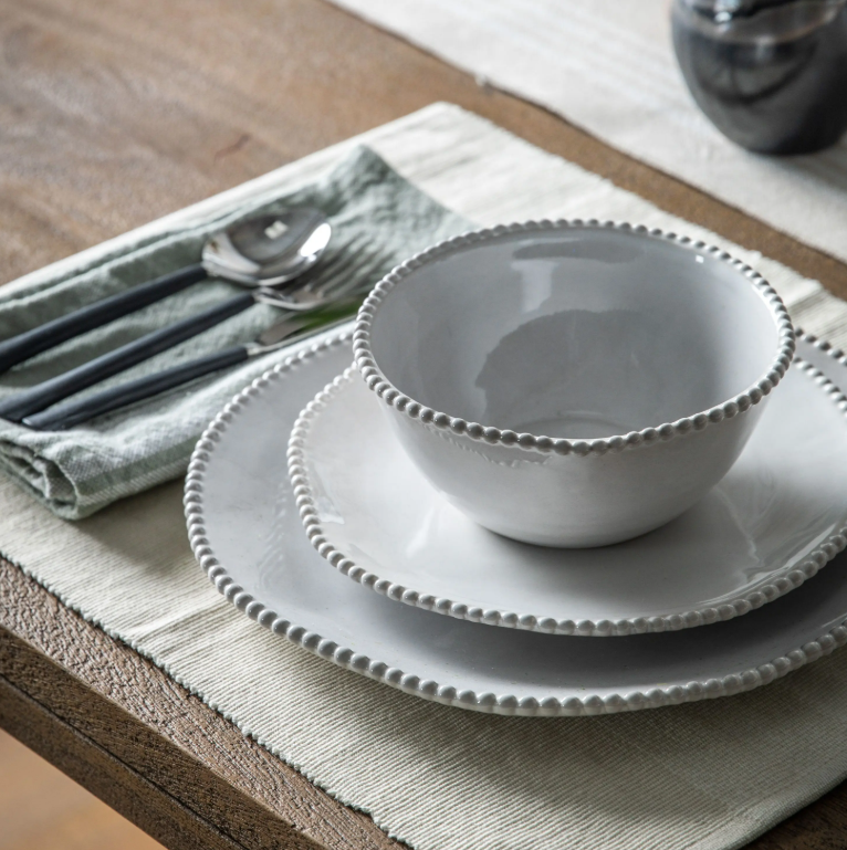 Set of white ceramic bowls on a wooden table with cutlery and a napkin.