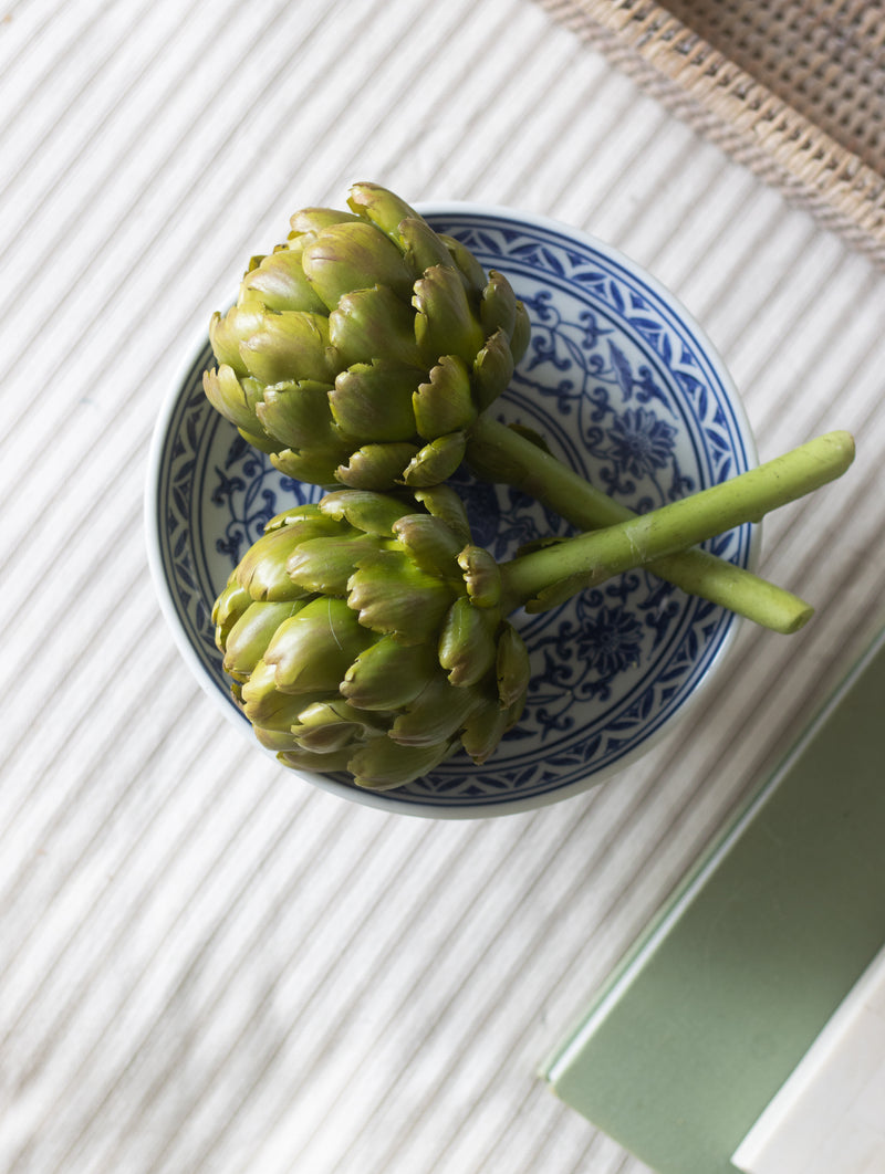 Two artichokes on a decorative blue and white plate on a textured surface.