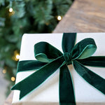 Gift box with a green ribbon in front of a Christmas tree