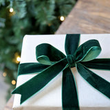 Gift box with a green ribbon in front of a Christmas tree
