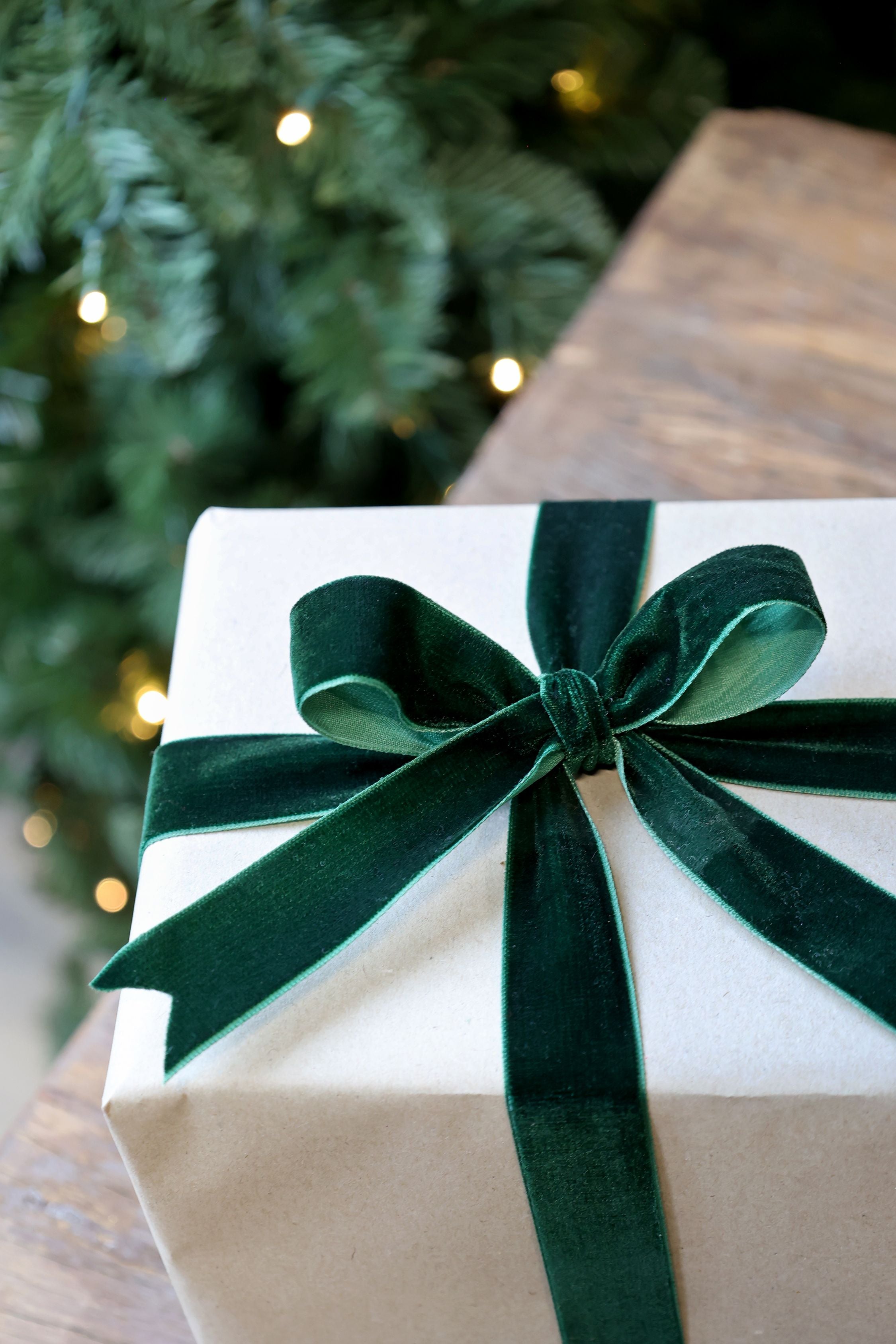 Gift box with a green ribbon in front of a Christmas tree