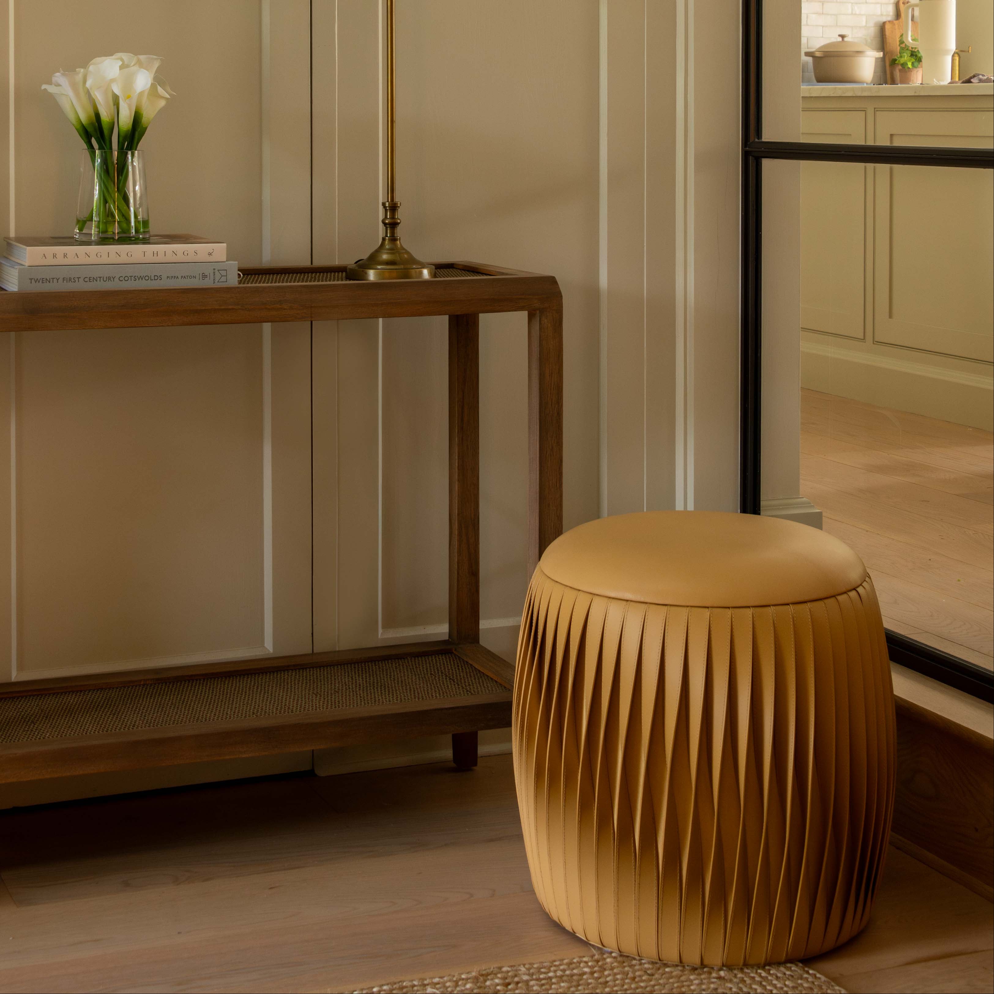 Modern interior with a wooden console table, gold lamp, and beige stool.