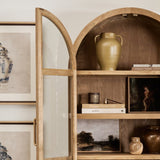 Wooden armoire with open doors displaying various items in a room with framed pictures and a plant.