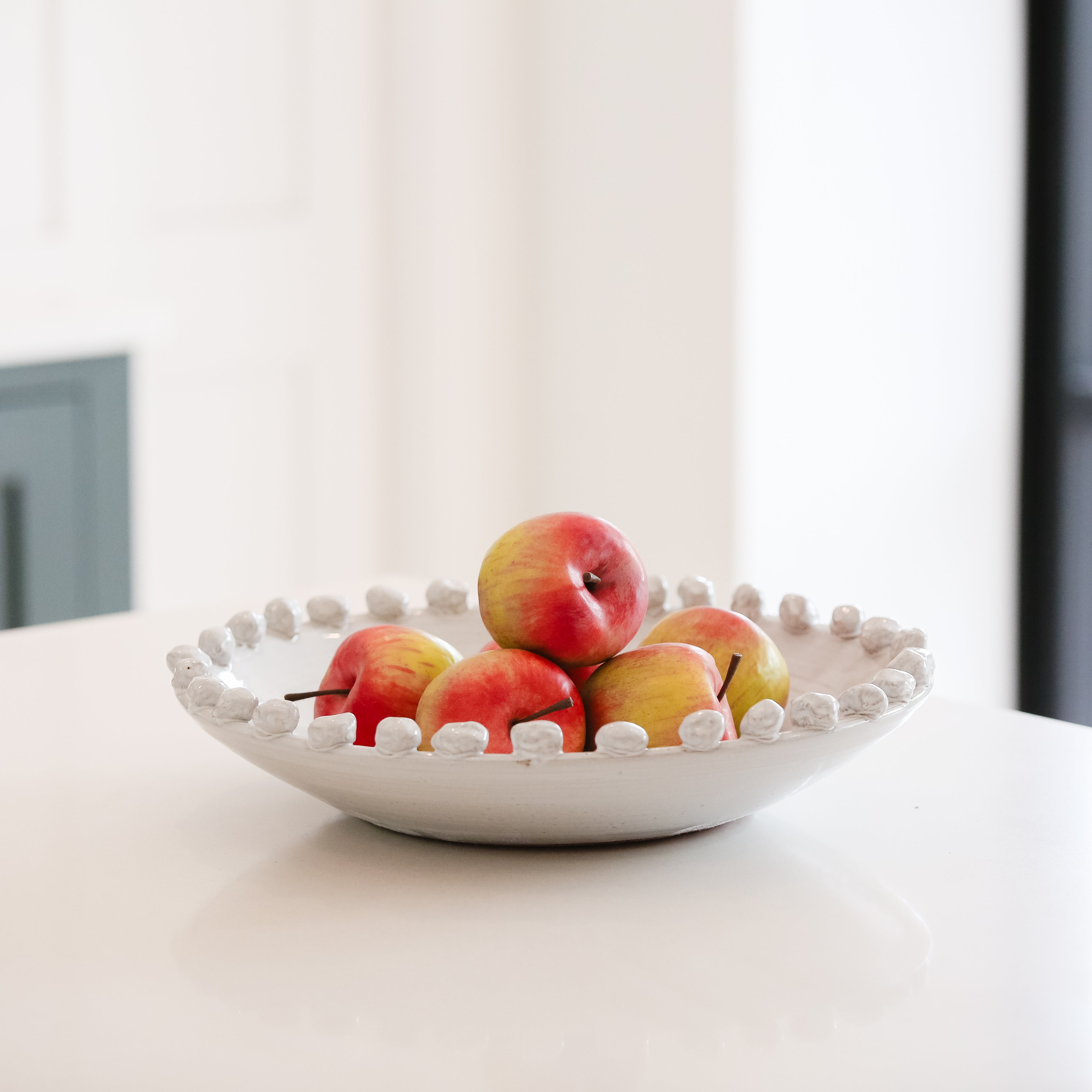 White decorative bowl holding a set of lifelike faux Fuji apples in red and yellow tones