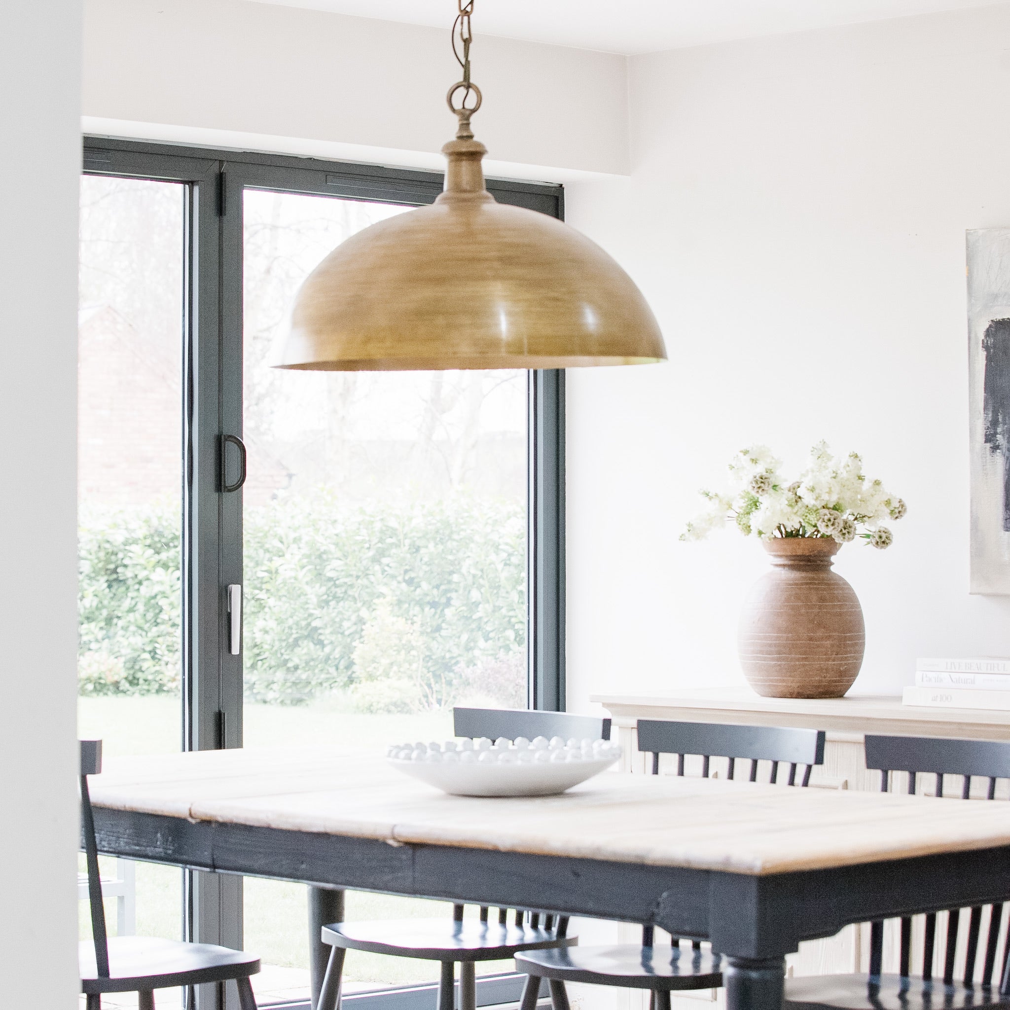 An oversized pendant light with a bronze finish hanging over a dining table in a room with a light color scheme.