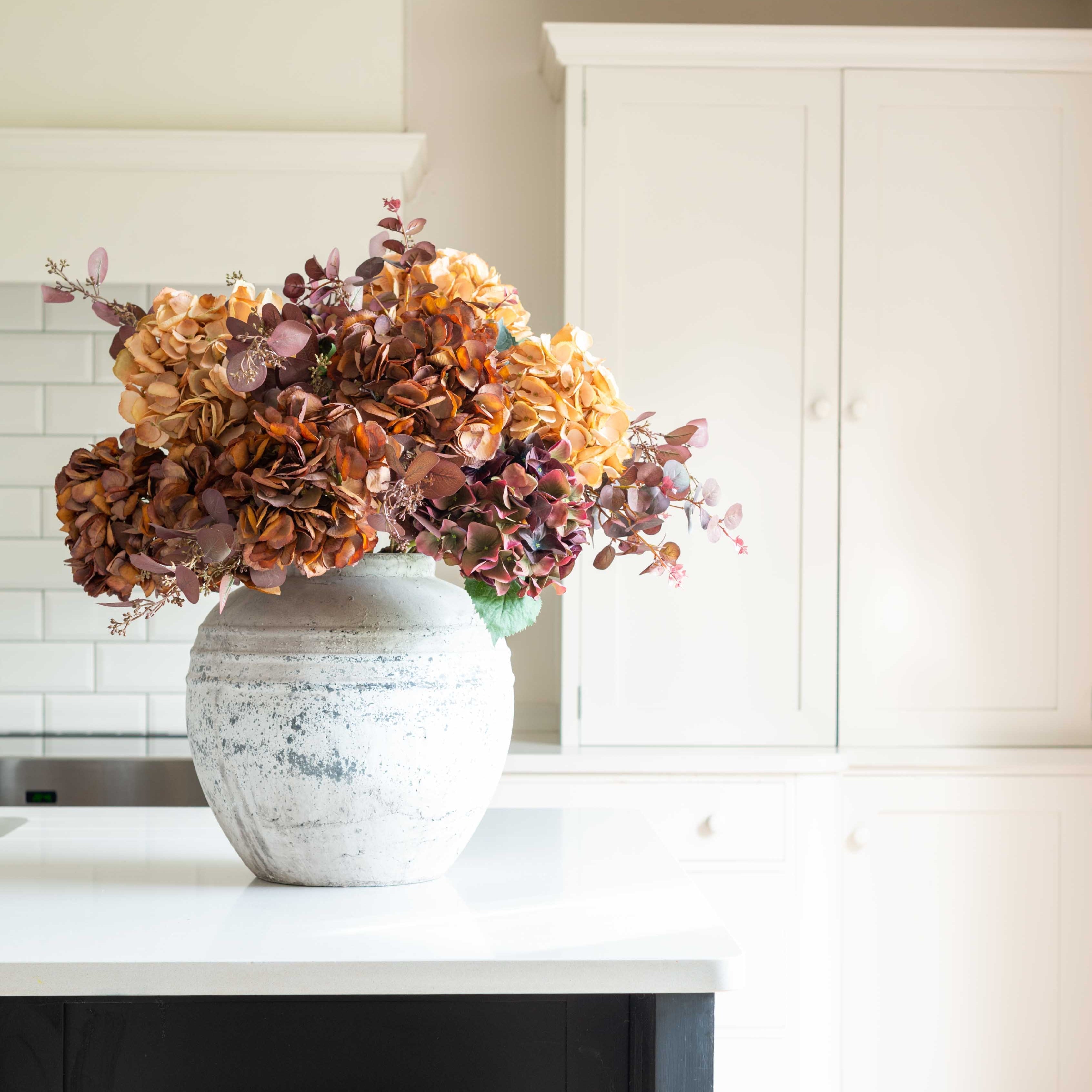 Stone pot with autumn floral arrangement on a white kitchen counter
