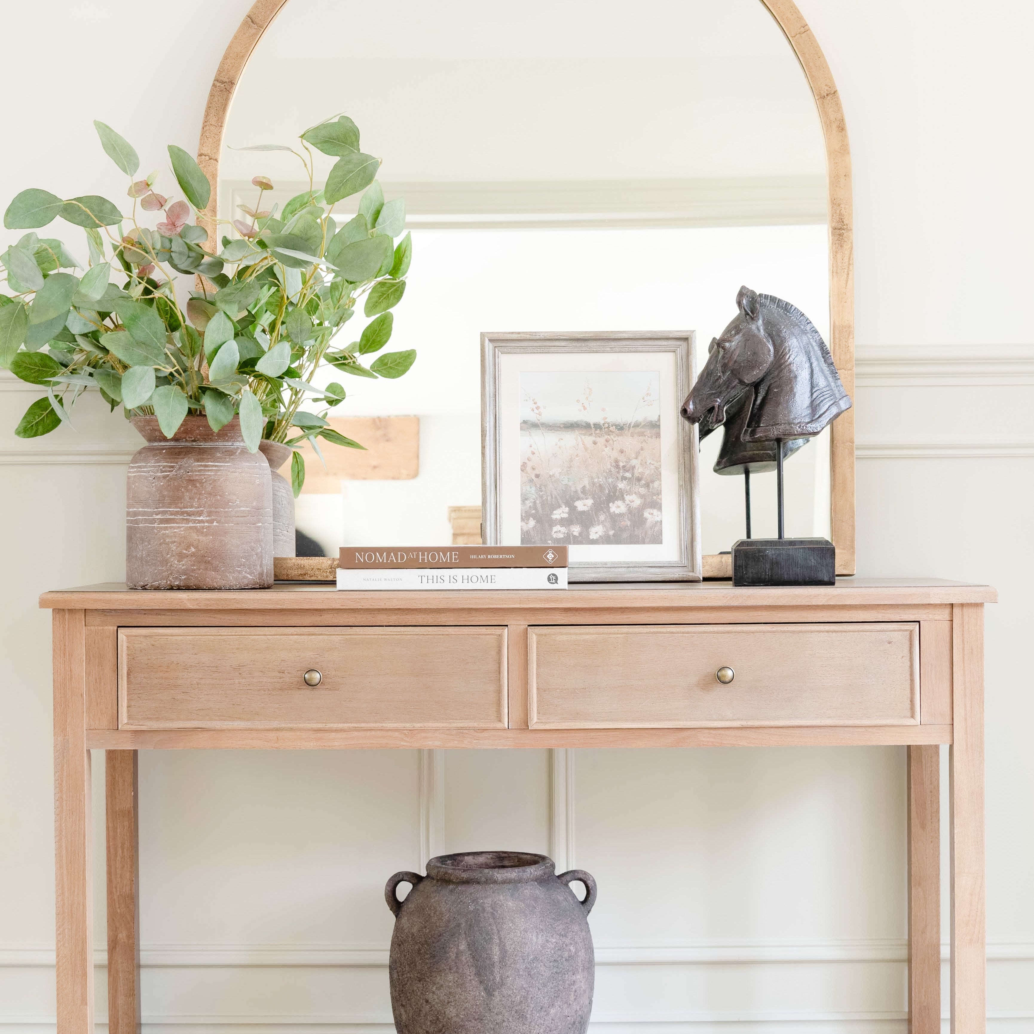 A stunningly crafted brass-framed arched top mirror. It sits on a pine console table.
