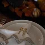 Gold bow napkin ring on a white plate with fall leaves and pumpkins in the background