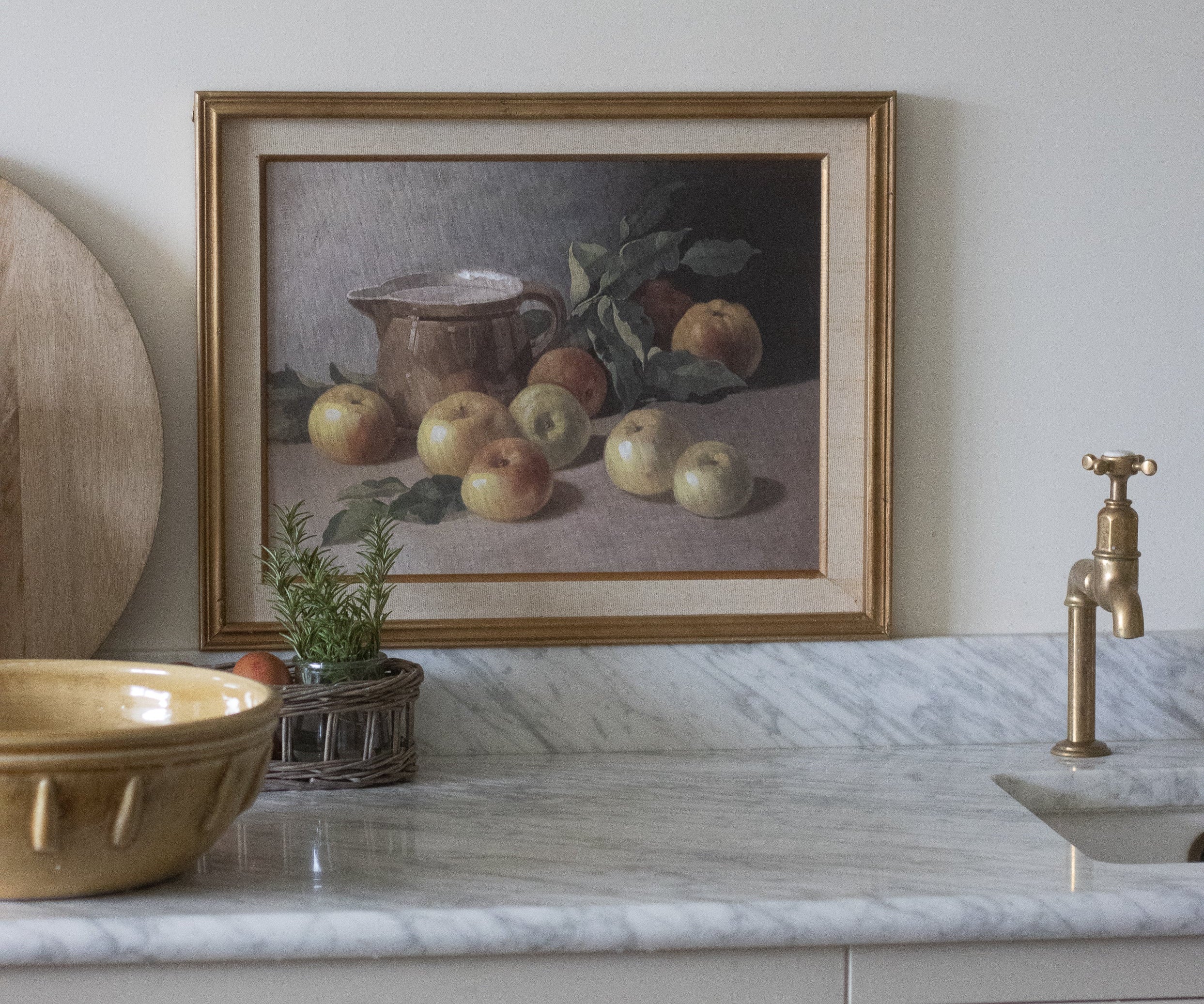 Kitchen counter with marble surface, gold bowl, and framed still life painting on wall.