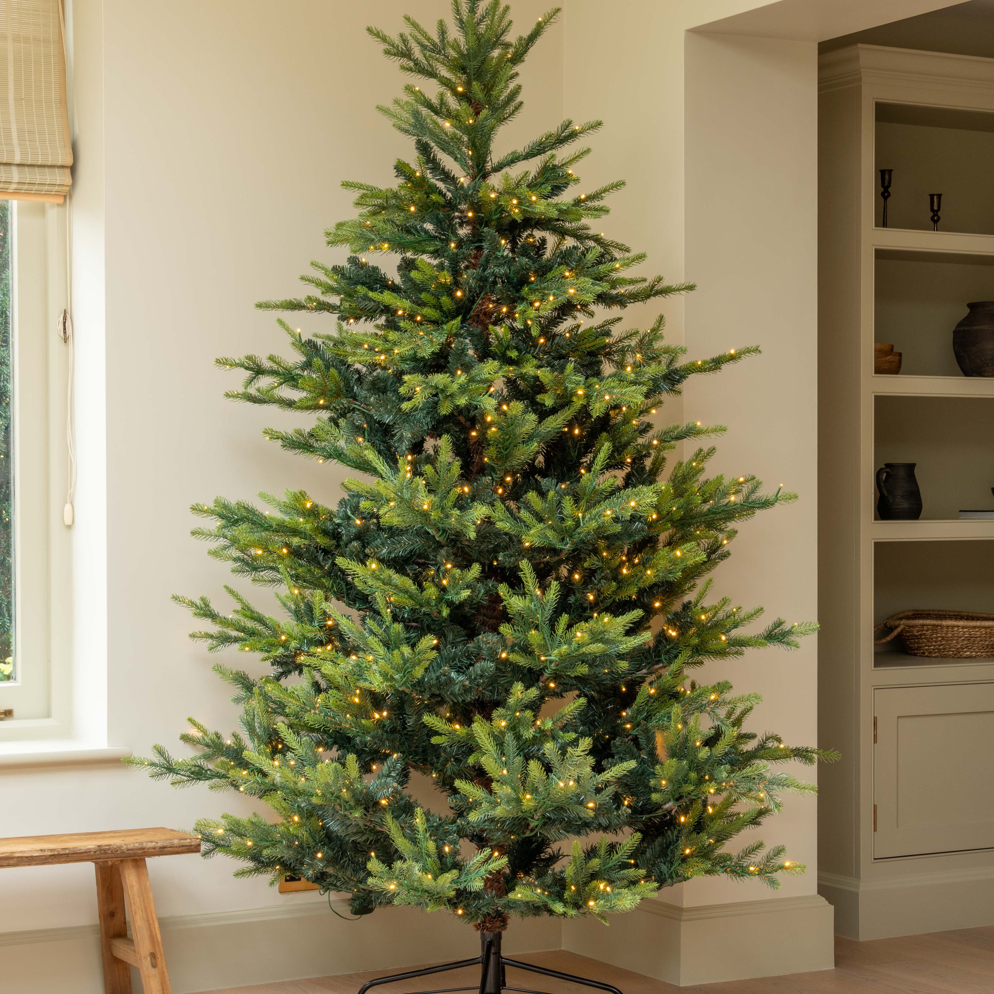 Decorated Christmas tree in a room with a window and shelves.