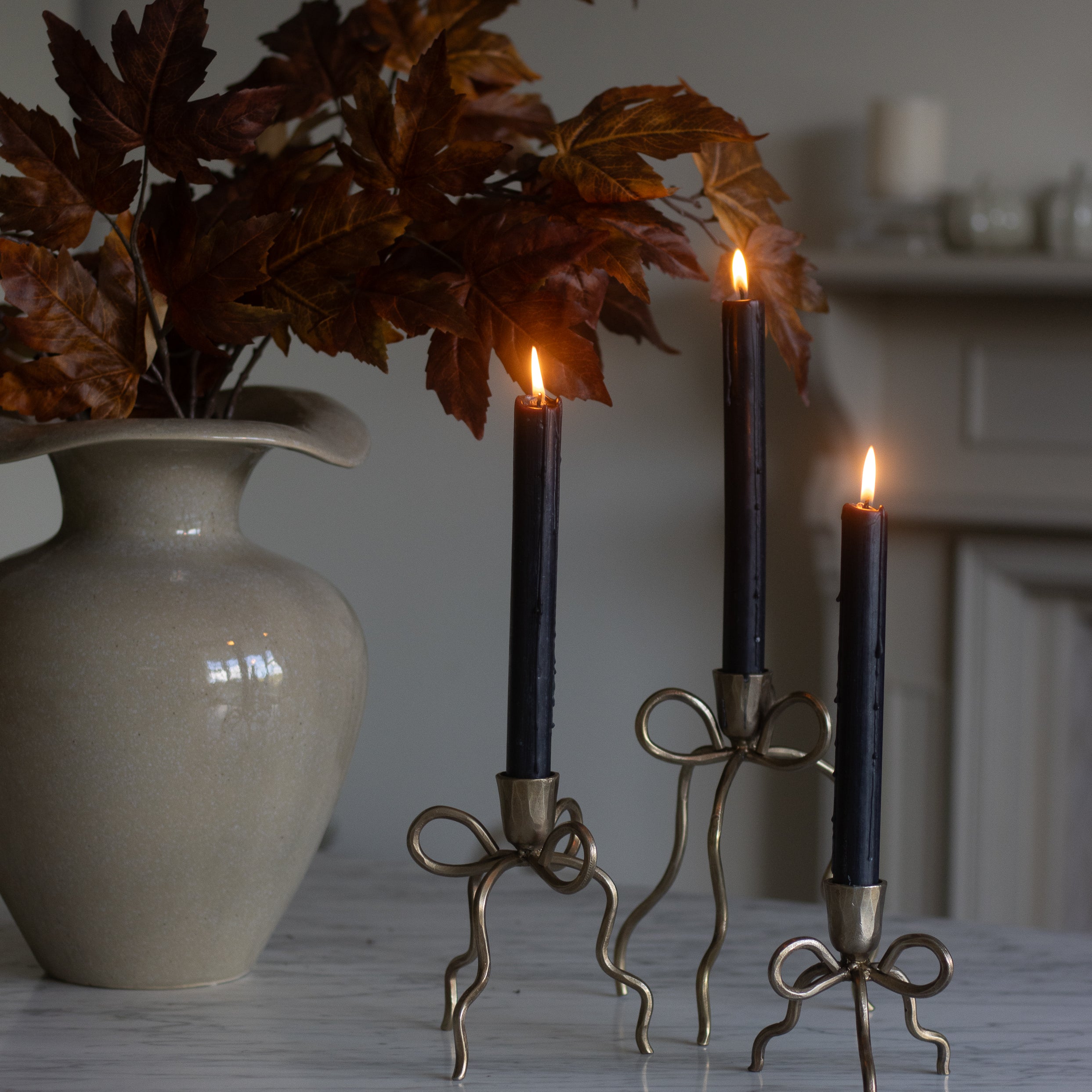 Decorative candle holders with lit candles next to a vase on a marble surface.