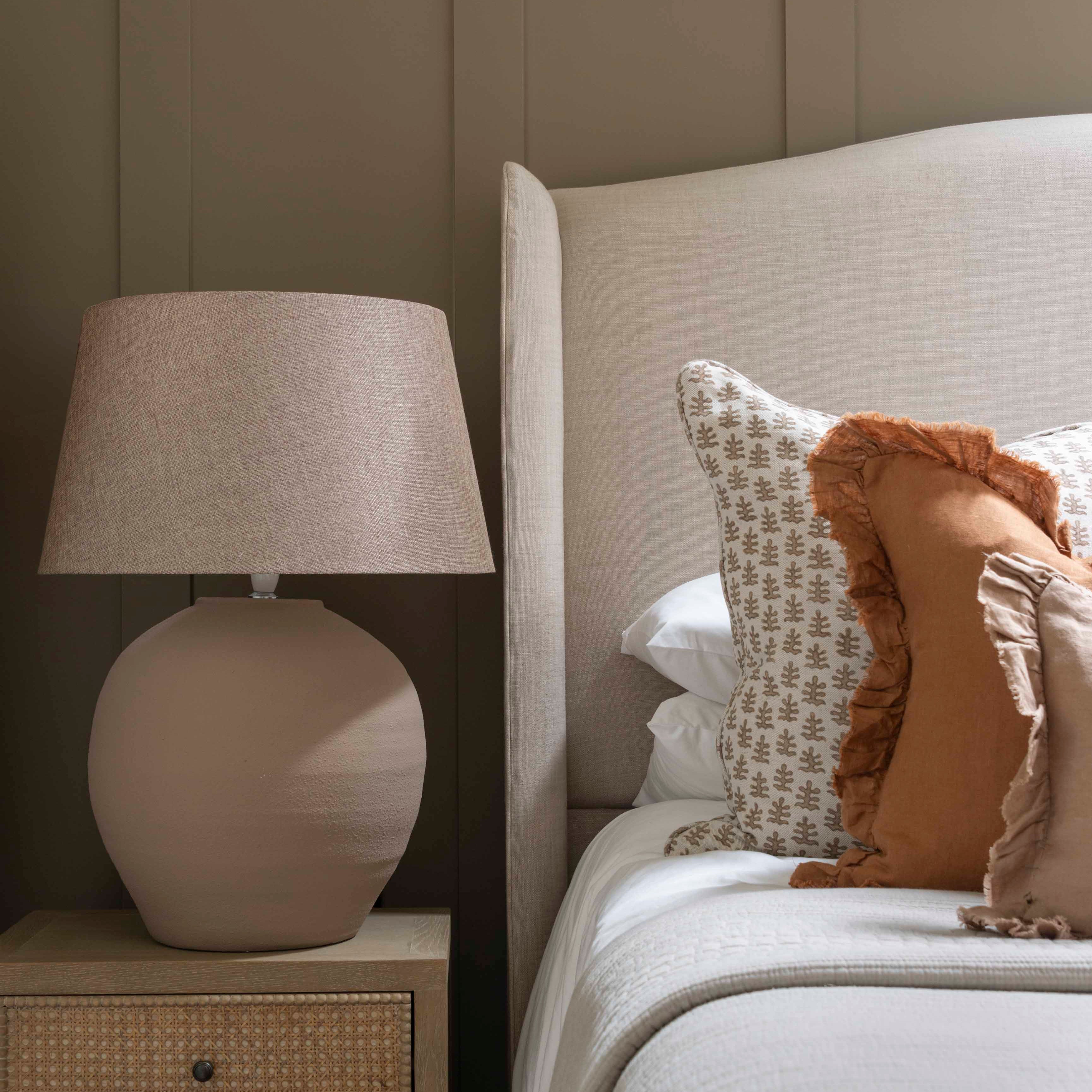 An elegant beige table lamp set by a bed.