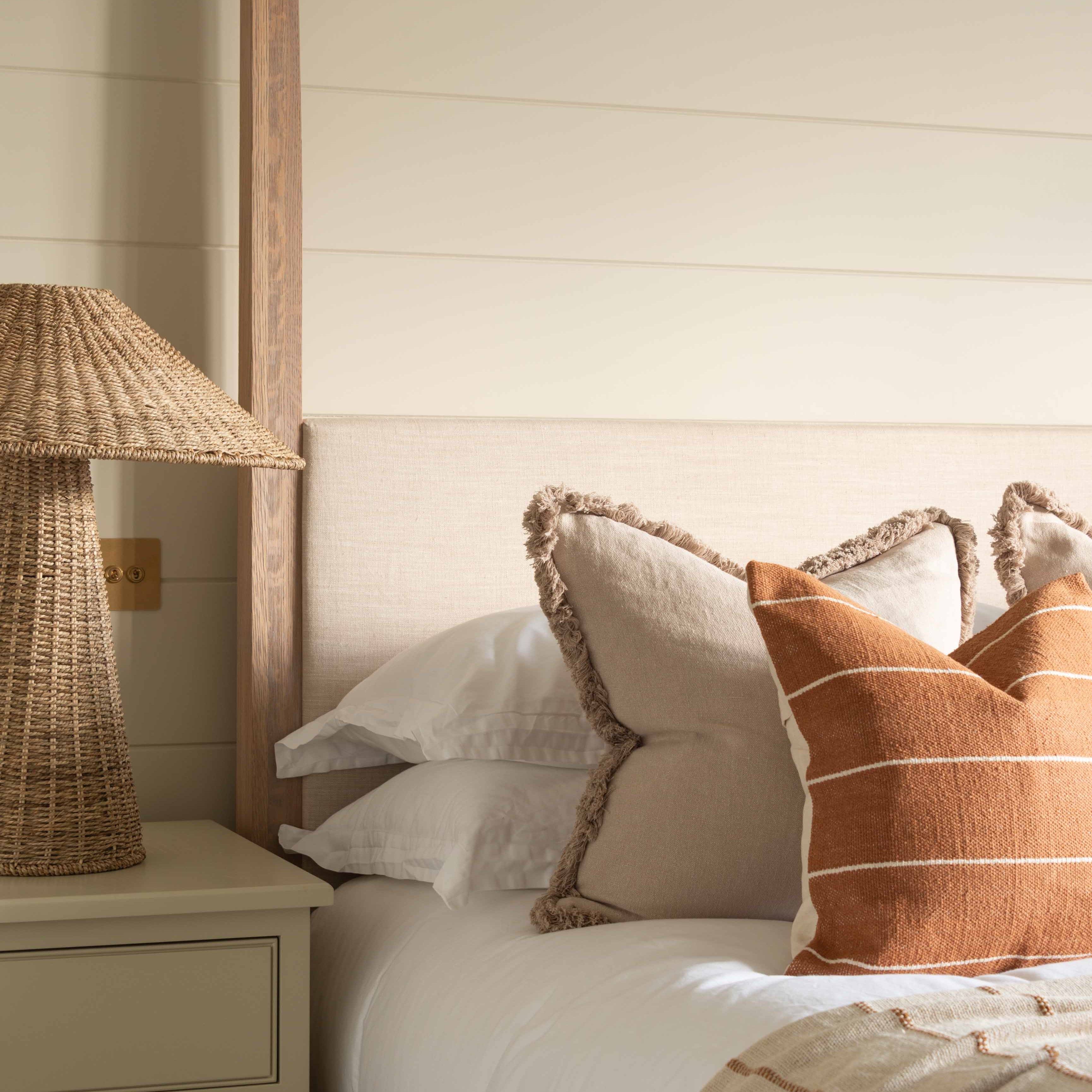 Rust textured cushion cover with ivory horizontal stripes displayed on a bed