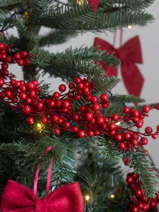 Faux red berry garland on a Christmas tree with a red bow