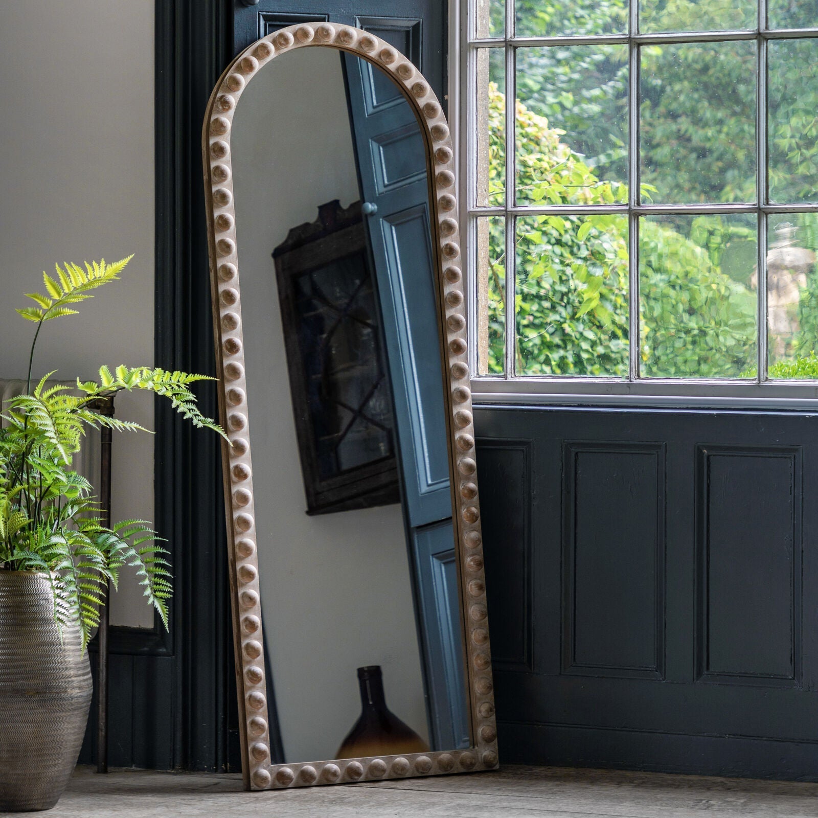 Arched full-length mirror styled in a rustic room with greenery and natural light