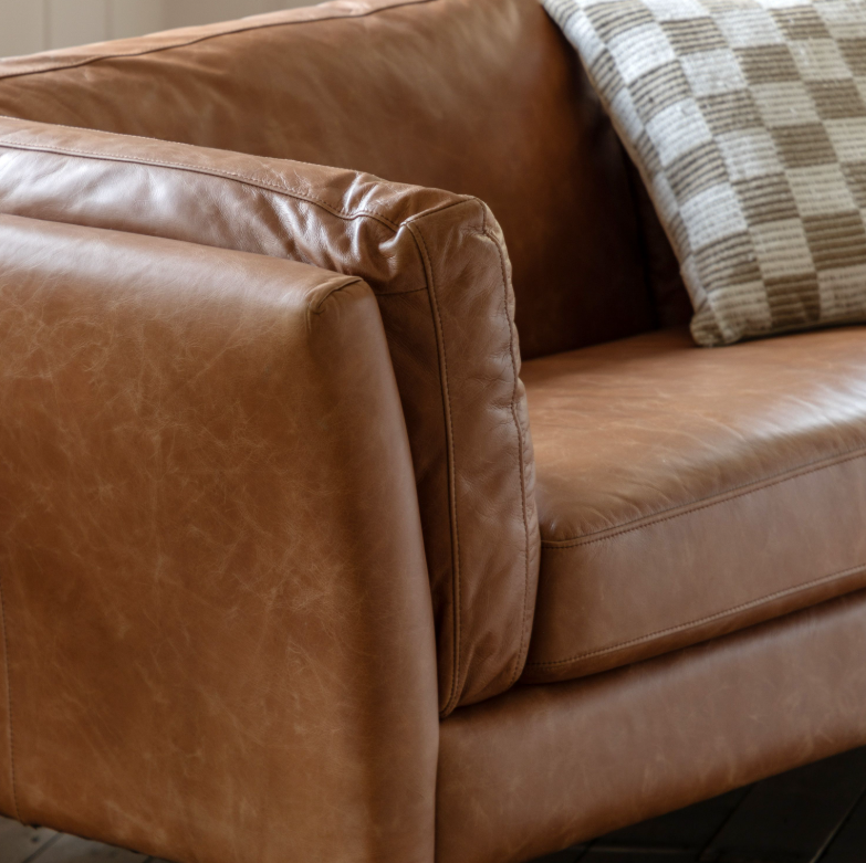 Brown leather sofa with a checkered pillow on a neutral background
