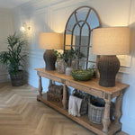 Wooden console table with lamps, plants, and decorative items in a room with a mirror and light fixture.