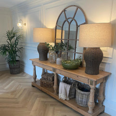 Wooden console table with lamps, plants, and decorative items in a room with a mirror and light fixture.