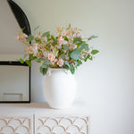 Elevate your home décor with the Athenia Textured White Ceramic Vase, a timeless piece inspired by classic Mediterranean amphora designs. Crafted with a minimalist matte white finish and a unique grainy texture, this vase features elegant looped handles that add sculptural charm to any space. Perfect for displaying dried florals or standing alone as a statement art object, the Athenia Vase seamlessly blends into modern, boho, or rustic interiors. Ideal for shelves, mantels, or console tables—bring home a to
