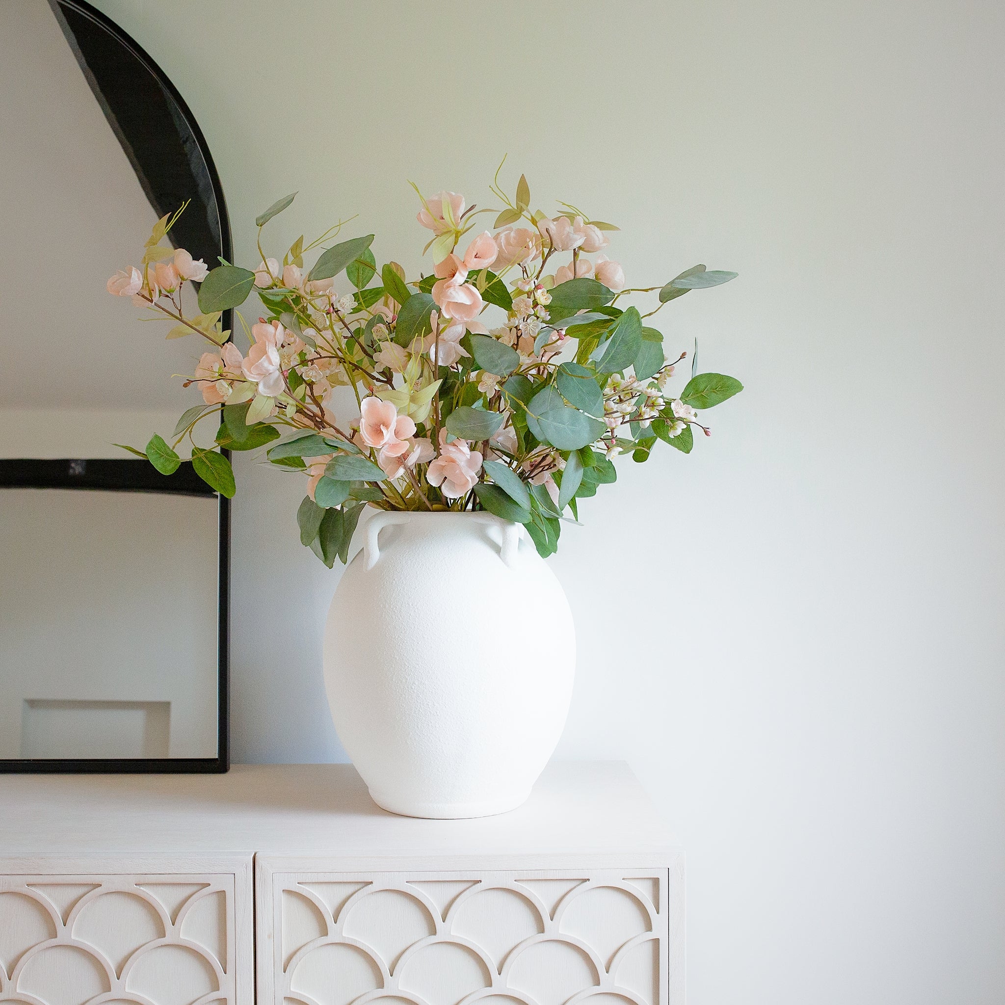 Elevate your home décor with the Athenia Textured White Ceramic Vase, a timeless piece inspired by classic Mediterranean amphora designs. Crafted with a minimalist matte white finish and a unique grainy texture, this vase features elegant looped handles that add sculptural charm to any space. Perfect for displaying dried florals or standing alone as a statement art object, the Athenia Vase seamlessly blends into modern, boho, or rustic interiors. Ideal for shelves, mantels, or console tables—bring home a to