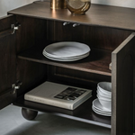 Wooden cabinet with open door displaying plates and a book on a neutral background