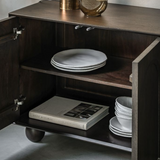 Wooden cabinet with open door displaying plates and a book on a neutral background