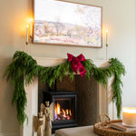 Decorated fireplace with greenery and a candle, framed artwork above, and a cozy living room setting.