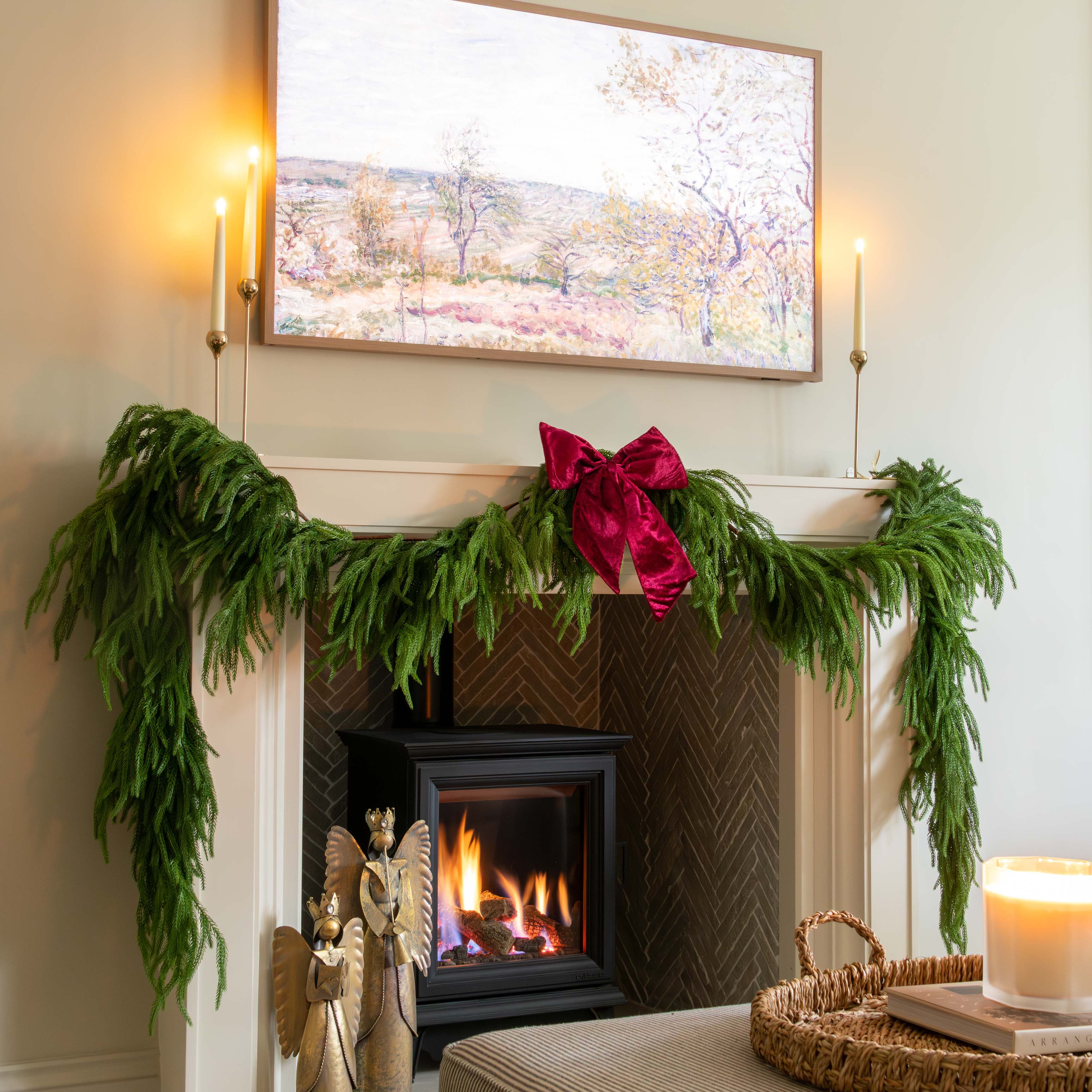 Decorated fireplace with greenery and a candle, framed artwork above, and a cozy living room setting.