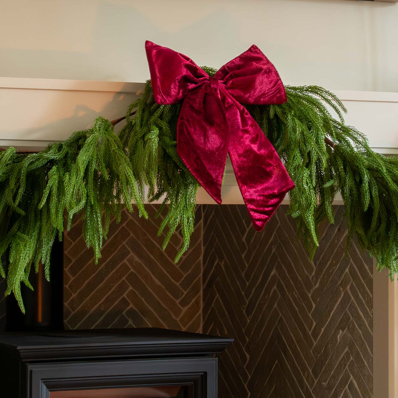 Green garland with a red velvet bow on a fireplace mantel.