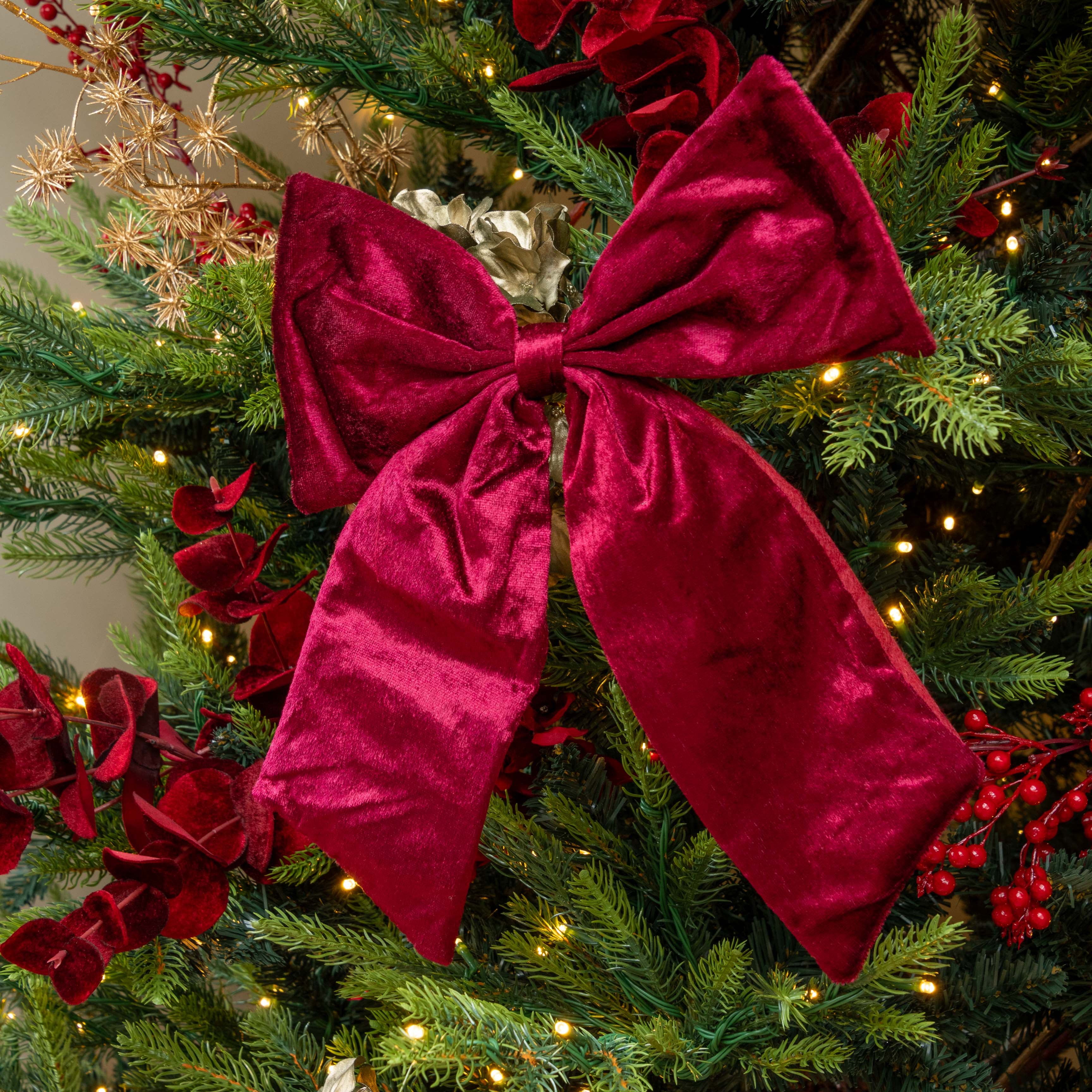 burgundy velvet bow on a decorated Christmas tree with lights and red berries.