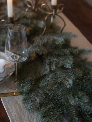 Faux noble pine garland on a dining table with glassware and brass candlesticks