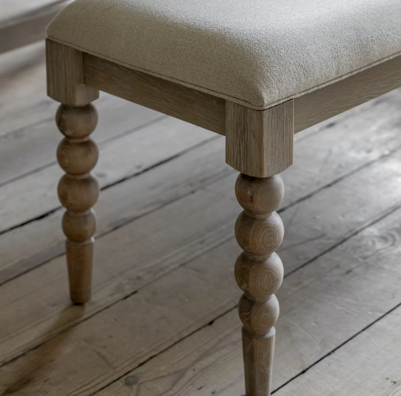Beige upholstered bench with turned wooden legs close up