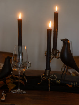 Candle holder with three lit candles on a table, featuring a glass and blackbird