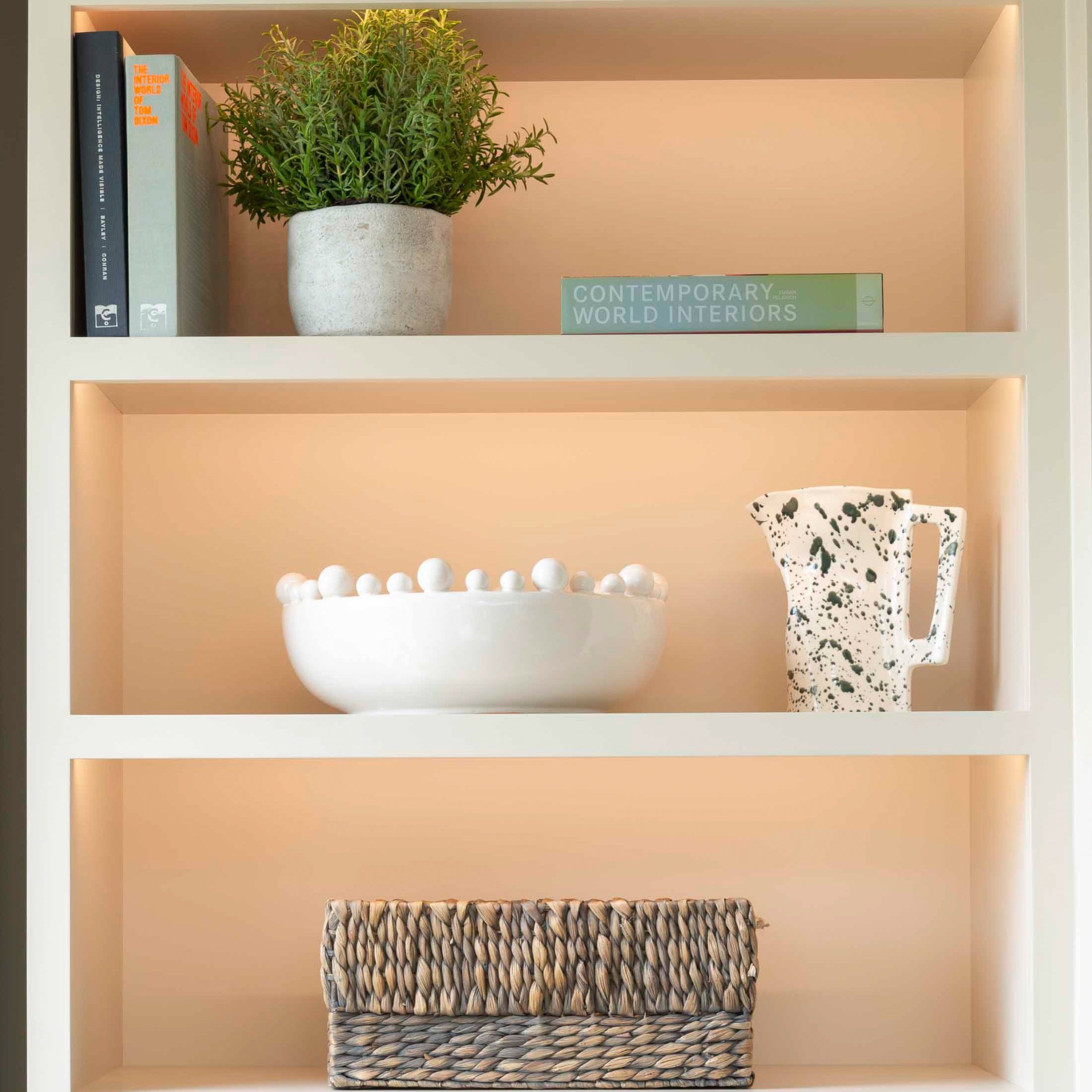 A white ceramic bowl with balls around the rim displayed on a shelf with other decorative items.