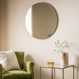 Round mirror on a wall above a green chair with a small table and plant in the foreground.