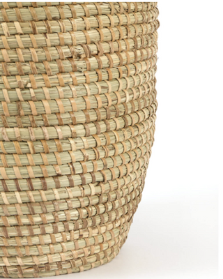 Close-up of a woven natural fiber basket in light tan and beige tones, showing the detailed texture of the hand-woven material against a plain white background.