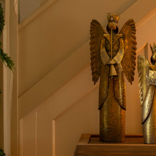 Decorative angel figurine with gold wings on a shelf next to books and a candle.