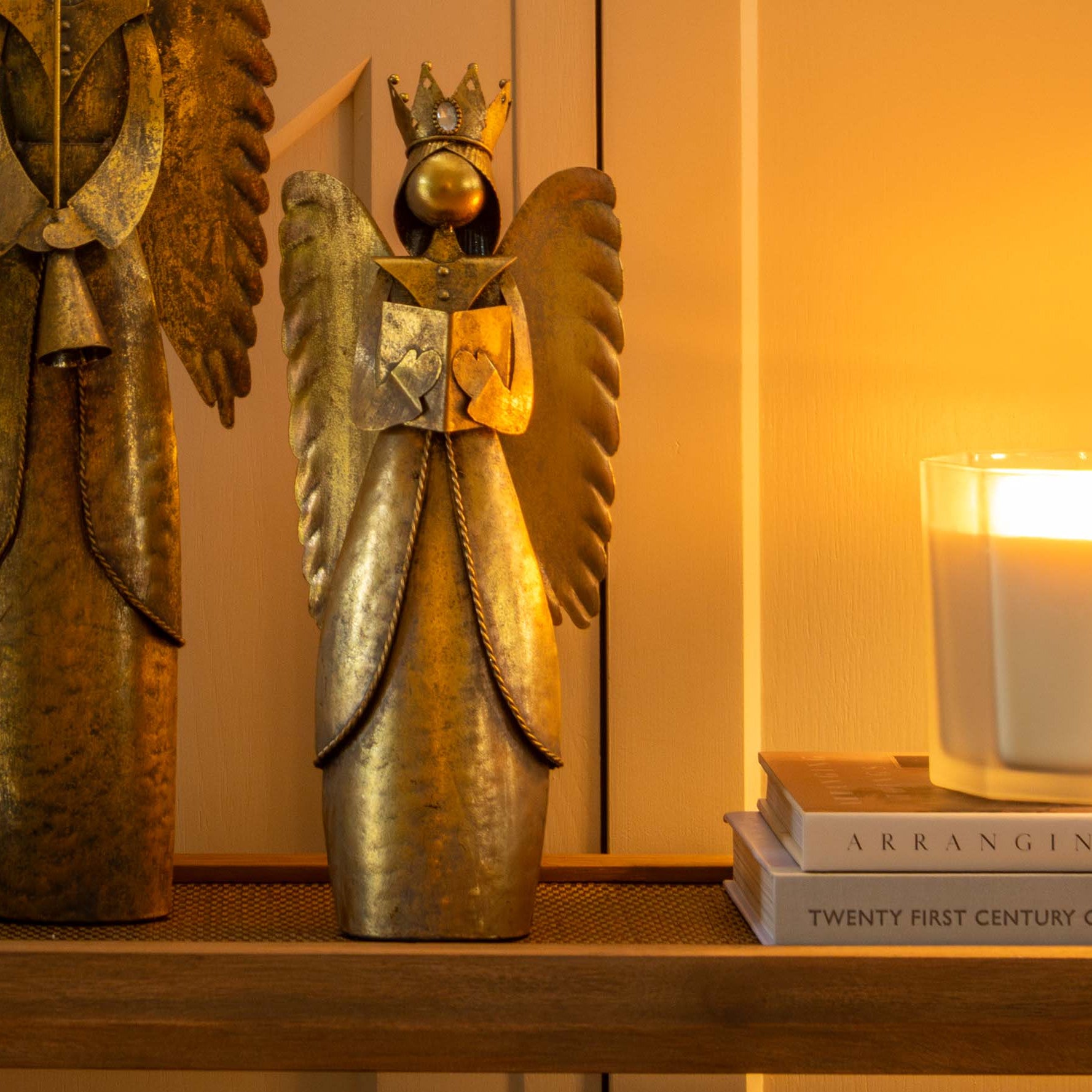 Decorative angel figurine with gold wings on a shelf next to books and a candle.