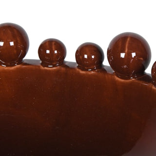 Close-up of a glossy dark brown ceramic surface with a row of raised rounded domes along the top edge, photographed against a white background.