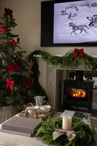 Deep red felt Christmas bow styled with greenery and warm white lights