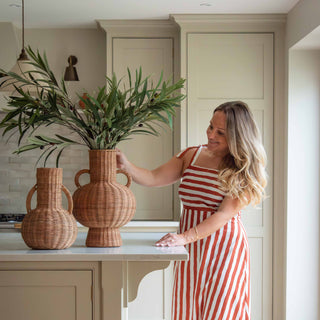 Woman in a red and white striped dress arranging plants in vases in a kitchen.