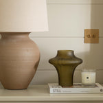 Decorative items including a lamp, vase, and candle on a shelf against a neutral wall.