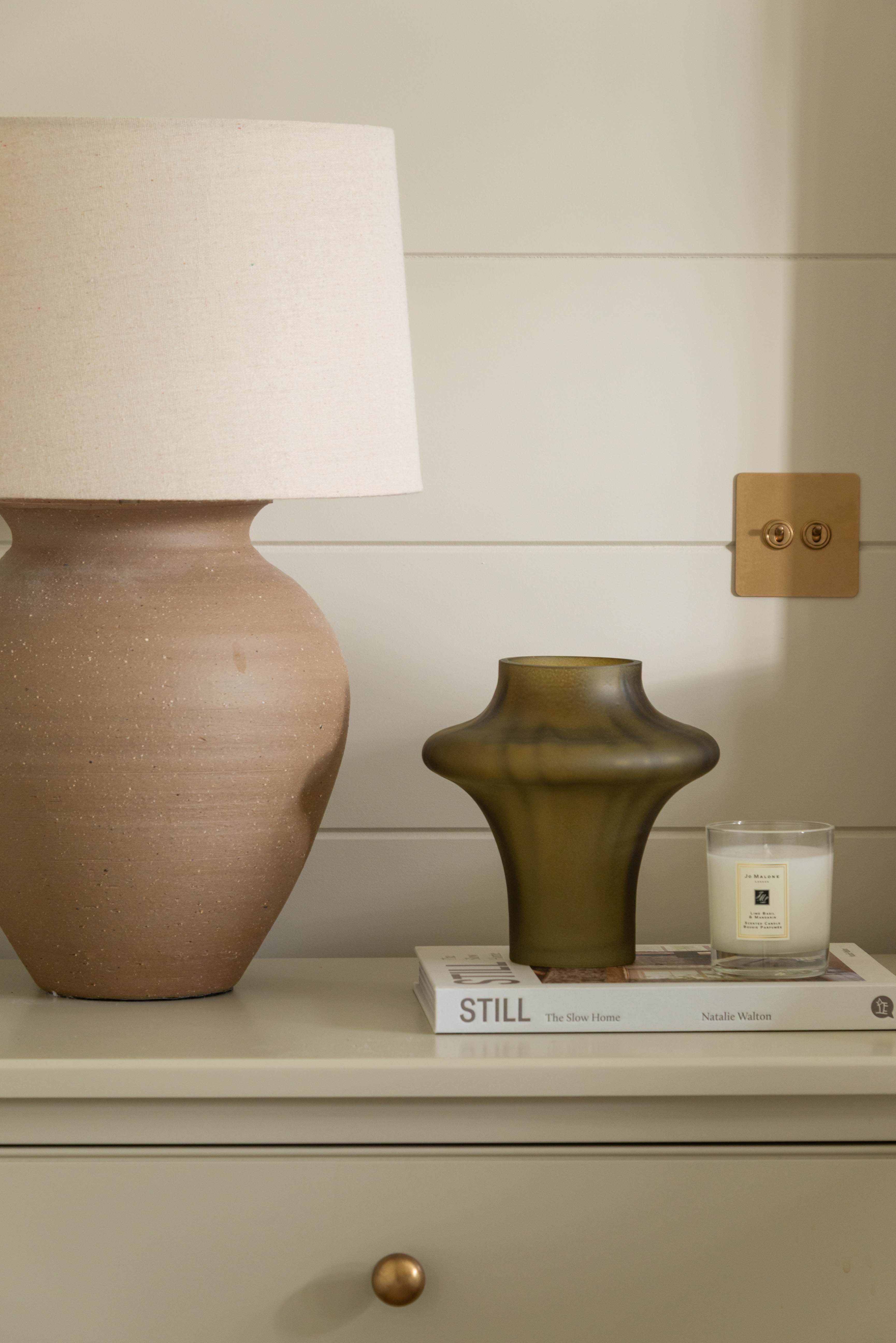 Decorative items including a lamp, vase, and candle on a shelf against a neutral wall.