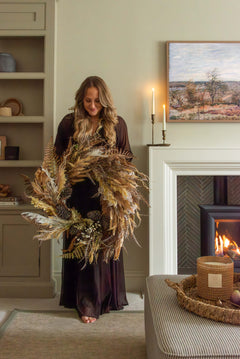 a premium autumnal wreath held my woman by fire in cosy living room