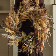 Woman holding a large dried wreath in a cozy living room with a fireplace.